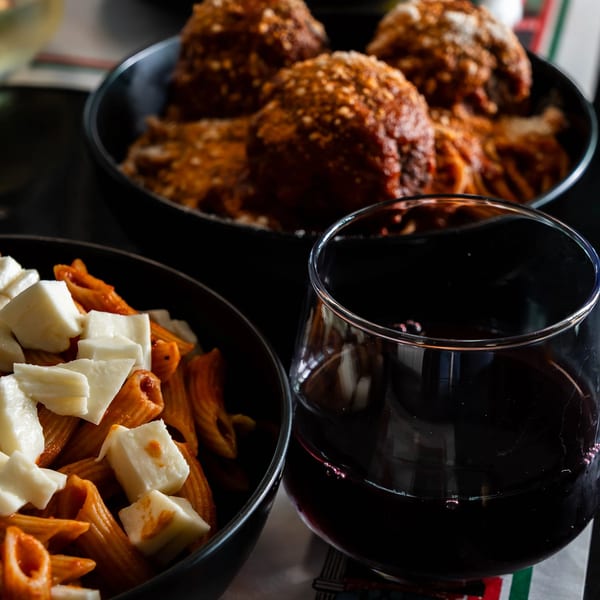 Bowls of pasta with mozzarella and meatballs, alongside glasses of red and white wine.