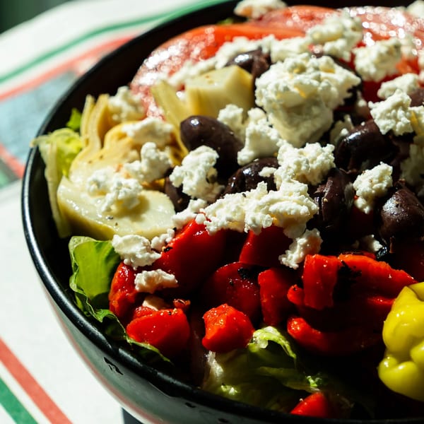 A vibrant salad with lettuce, roasted red peppers, olives, artichoke hearts, and feta cheese.