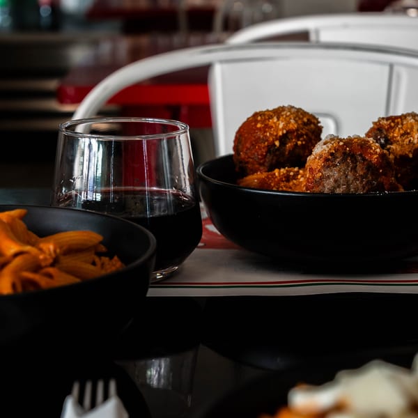 Bowls of meatballs and pasta, with a glass of red wine, on a restaurant table.