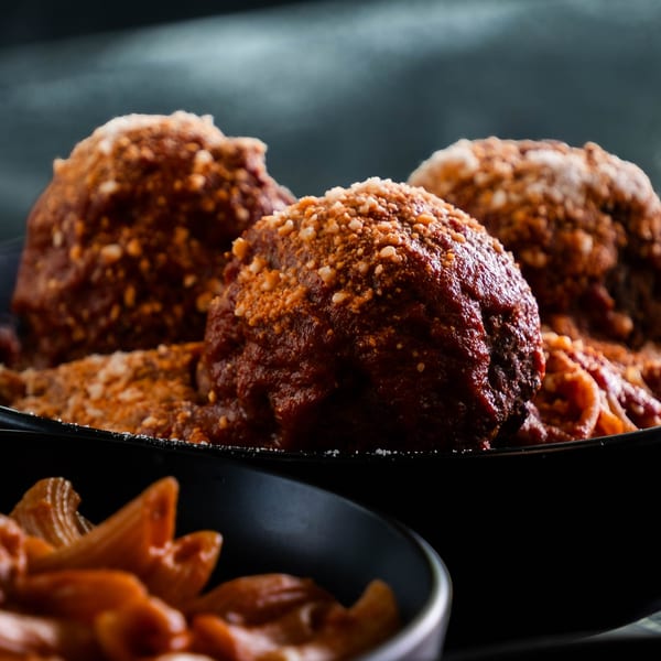 Three large meatballs covered in sauce and parmesan cheese, with pasta in the foreground.
