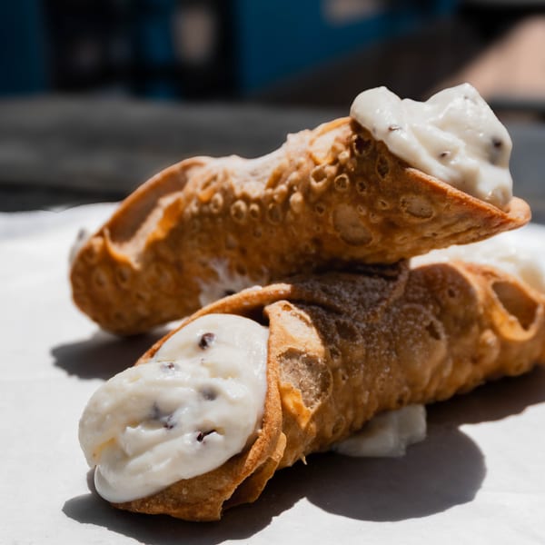 Two crispy cannolis with creamy white filling and chocolate chips on white paper.
