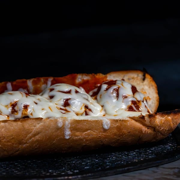 A toasted meatball sub with melted mozzarella cheese and marinara sauce on a dark background.