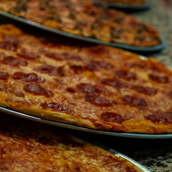 Close-up of several pizzas in metal pans, including cheese, pepperoni, and meat toppings.