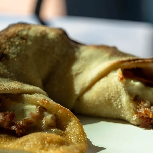Two golden-brown calzones, one cut open to reveal melted cheese and meat fillings.